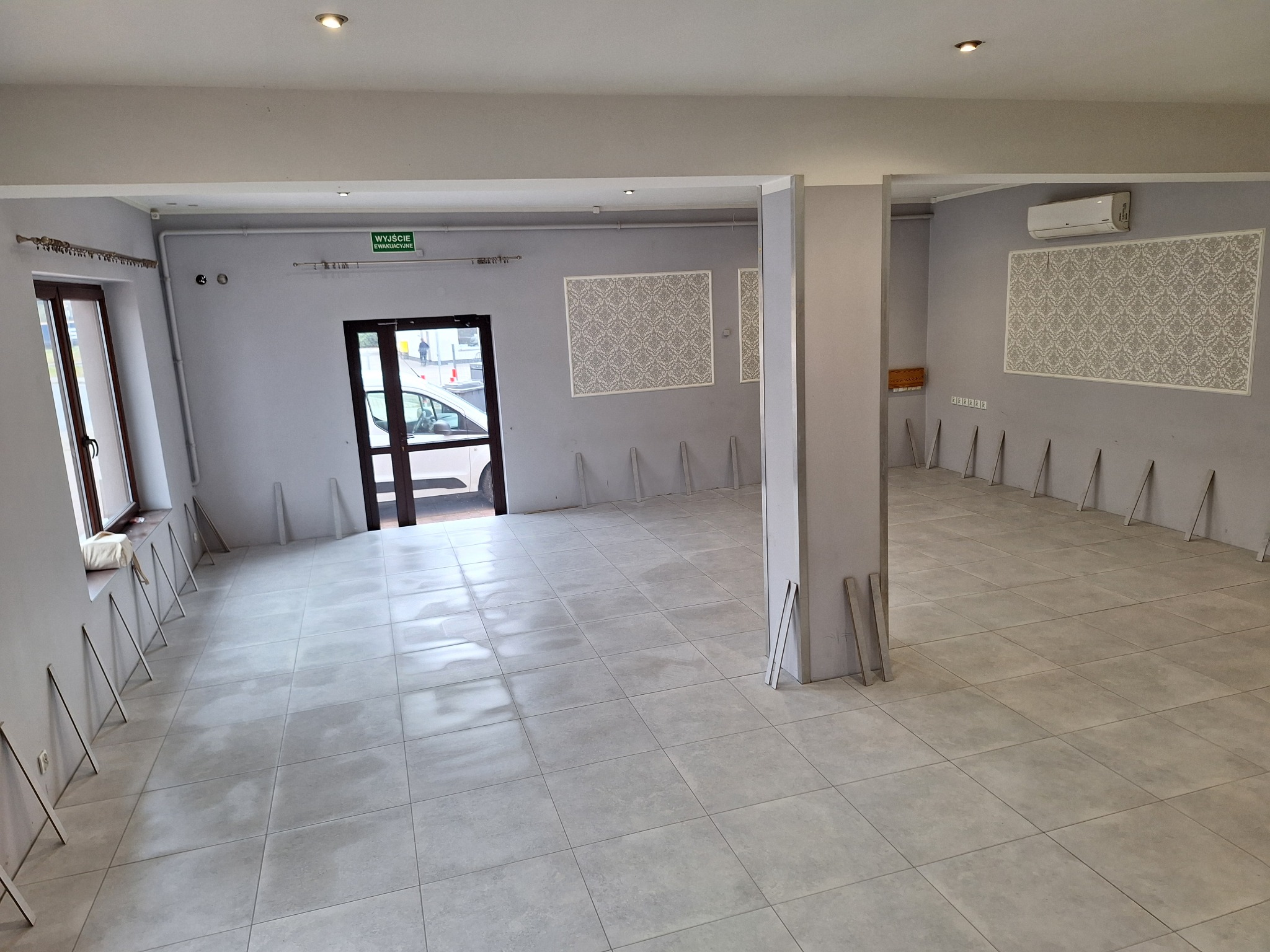 Wnętrze przestronnego lokalu po remoncie, z nową szarą podłogą z płytek, świeżo pomalowanymi szarymi ścianami, dekoracyjnymi panelami na ścianach i przygotowanymi listwami przypodłogowymi...