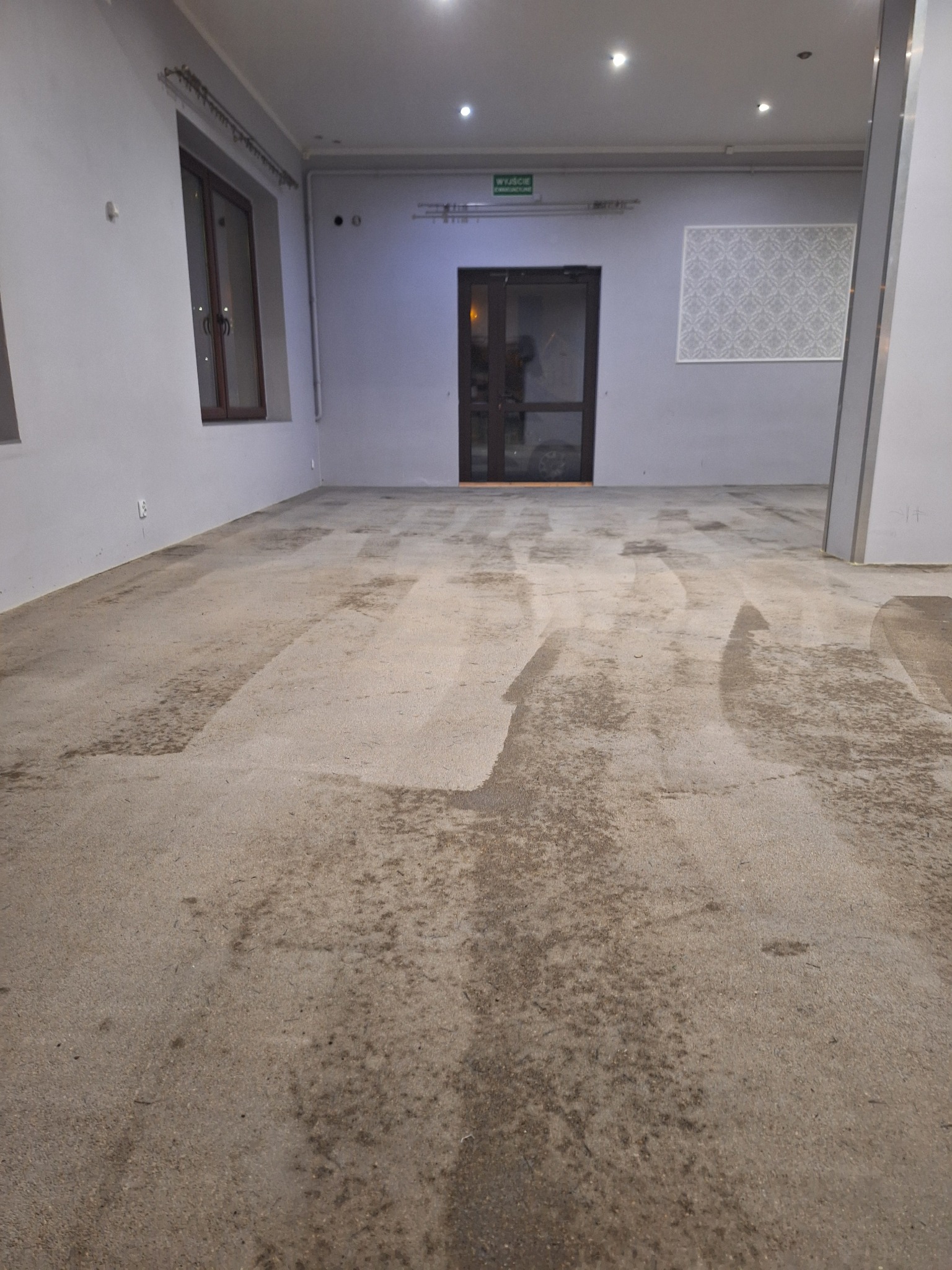 Przygotowanie podłoża pod wylewkę samopoziomującą w pustym pomieszczeniu, widoczne ślady po szlifowaniu betonu i odkurzaniu.