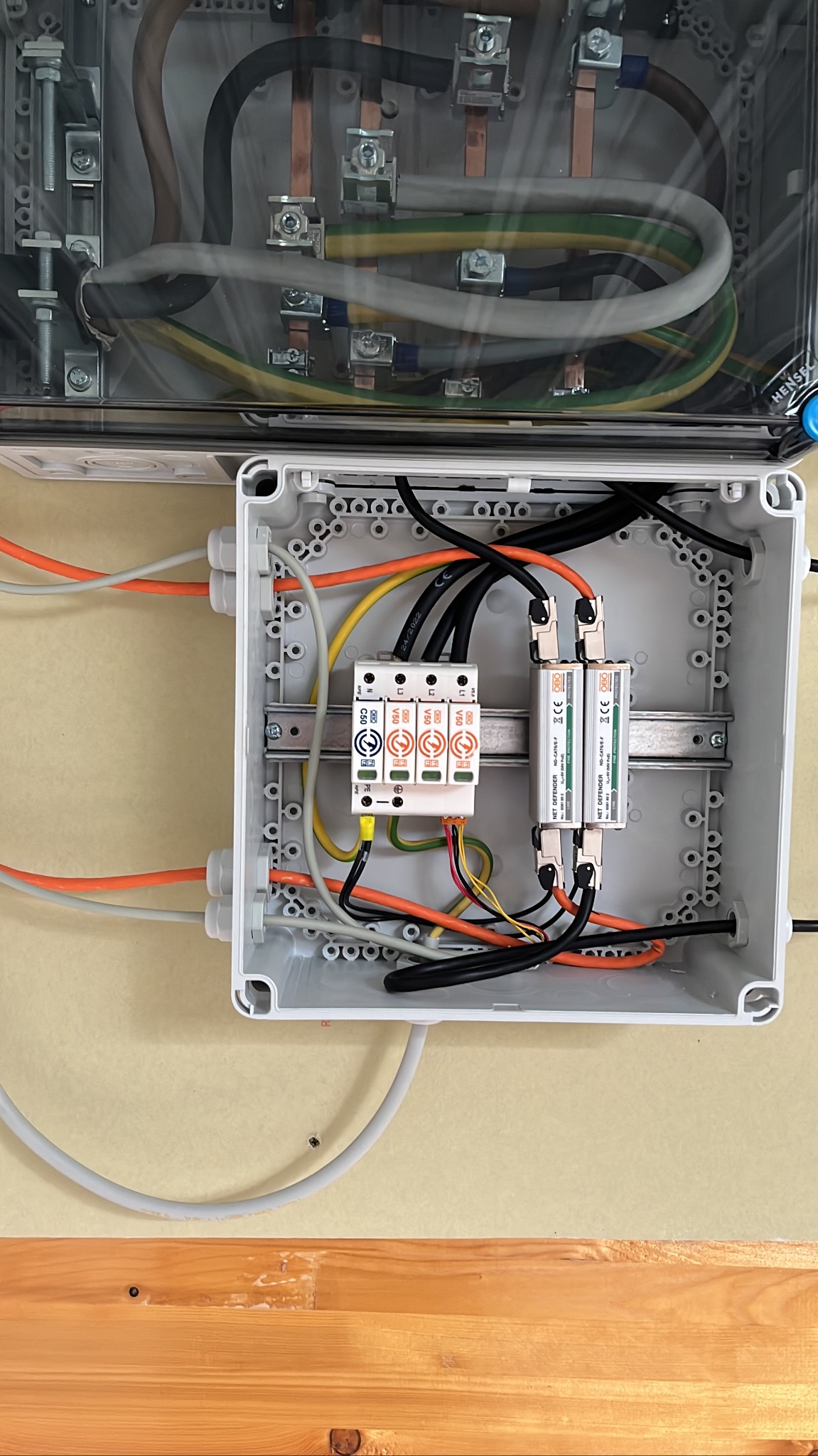 Rozdzielnica elektryczna z zabezpieczeniami przepięciowymi, widoczne przewody w różnych kolorach, zamontowane moduły ochronne oraz górna część skrzynki z przewodami przyłączonymi do listew...