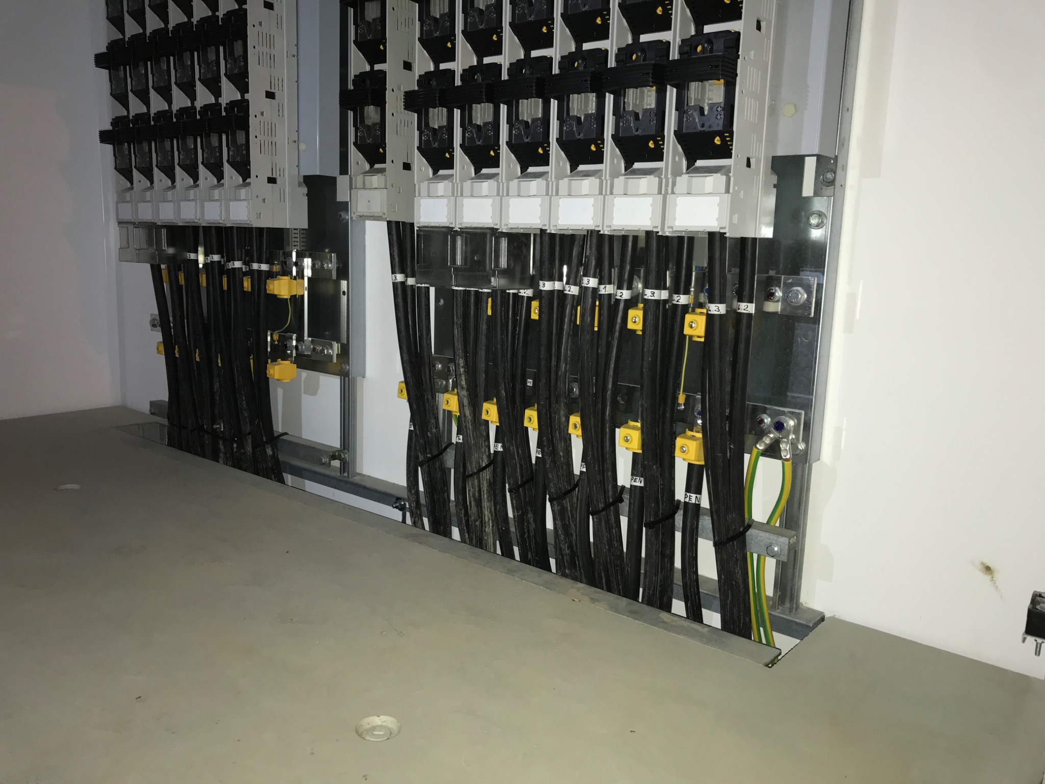 Rozdzielnia elektryczna z uporządkowanymi kablami, oznaczonymi etykietami i przymocowanymi do metalowej ramy, widoczne połączenia uziemiające.