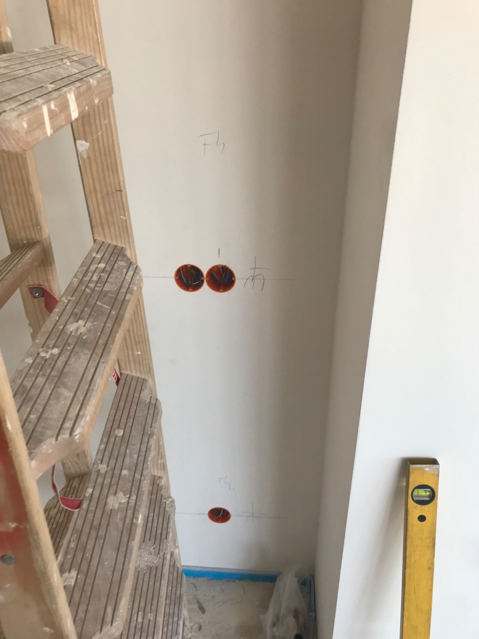 Wewnętrzna ściana z zaznaczonymi miejscami pod gniazdka elektryczne, widoczna drabina malarska i poziomica. Ślady ołówka na ścianie.