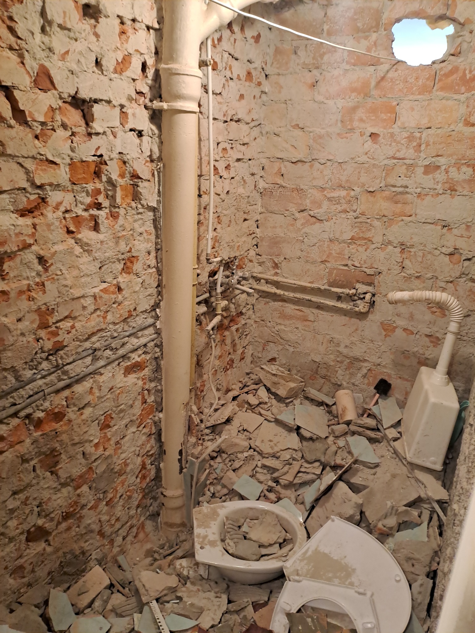 Demontaż starej toalety w trakcie remontu łazienki, widoczne gruz, odsłonięta cegła, rury i fragment otworu w suficie.