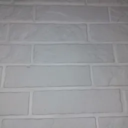 Biała ściana z cegły dekoracyjnej z wyraźną fakturą i spoinami, oświetlona z góry.