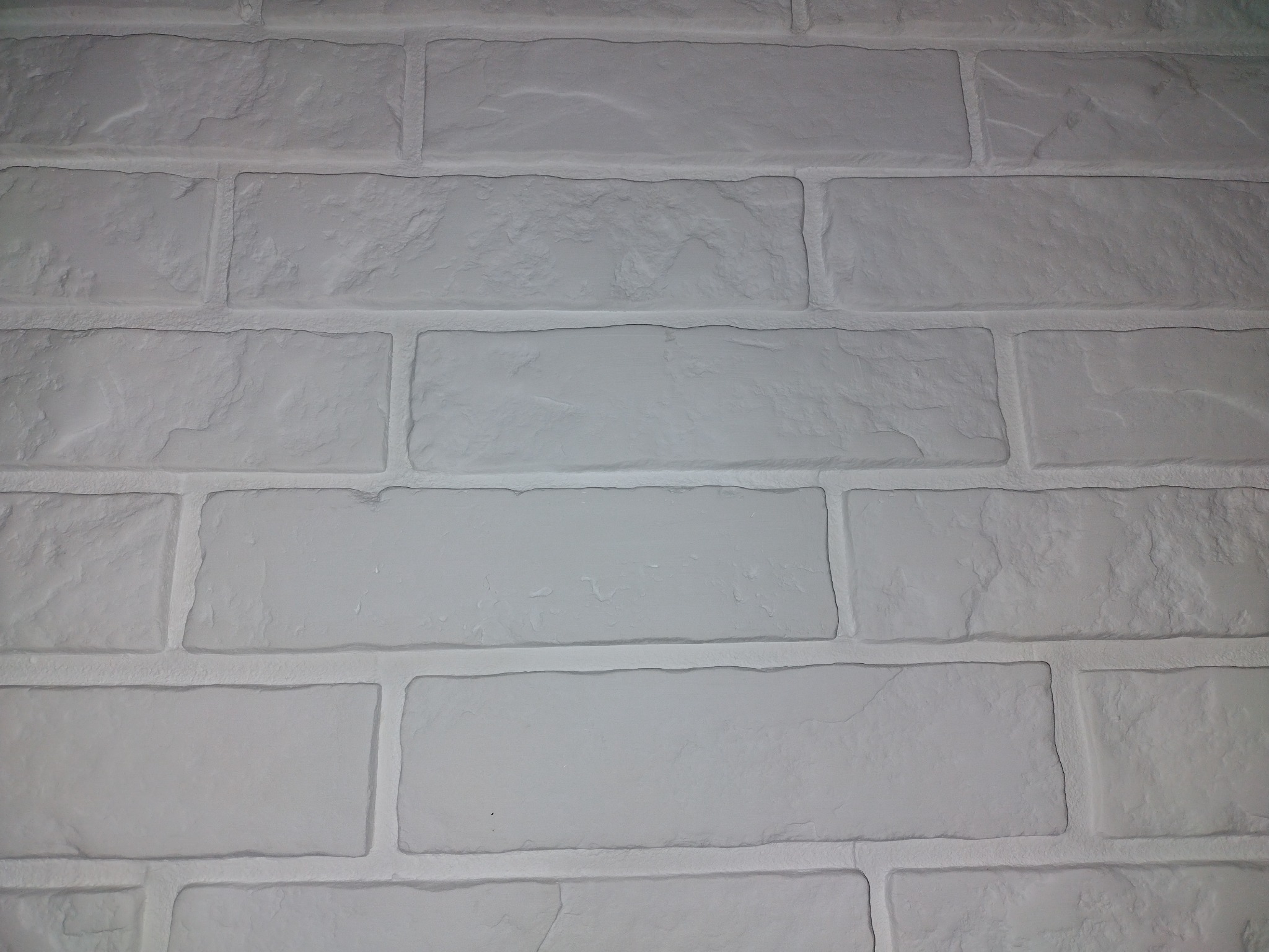 Biała ściana z cegły dekoracyjnej z wyraźną fakturą i spoinami, oświetlona z góry.