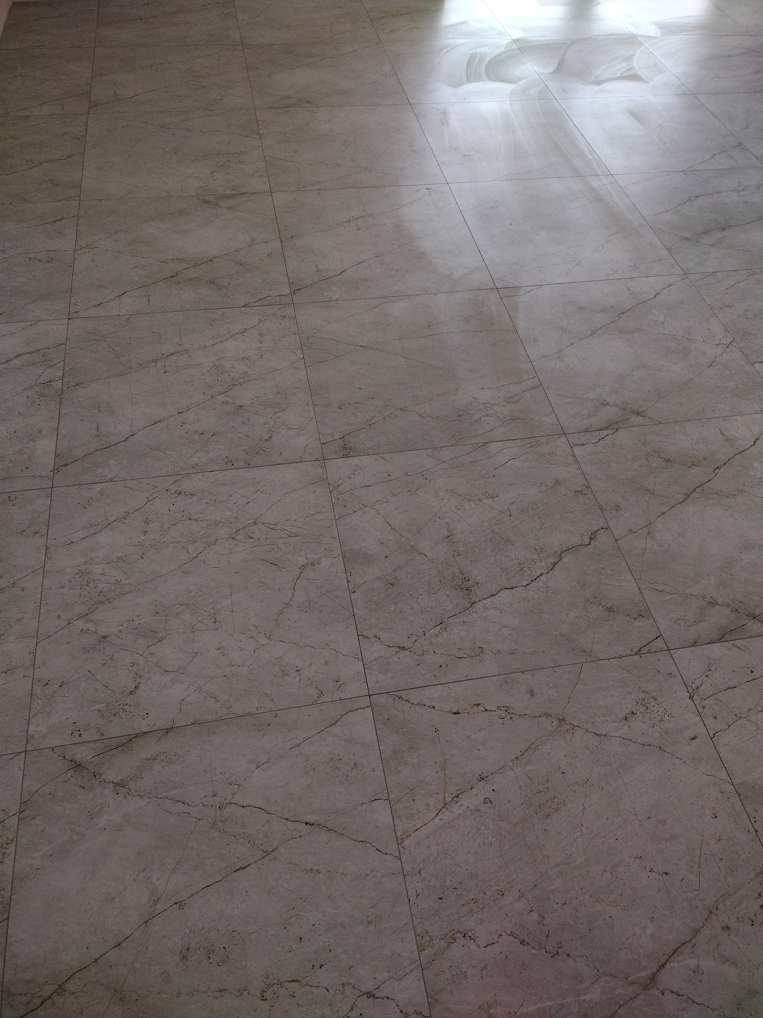 Szare, marmurowe płytki podłogowe ułożone w kwadratową siatkę, z widocznym odbiciem światła w górnej części kadru.