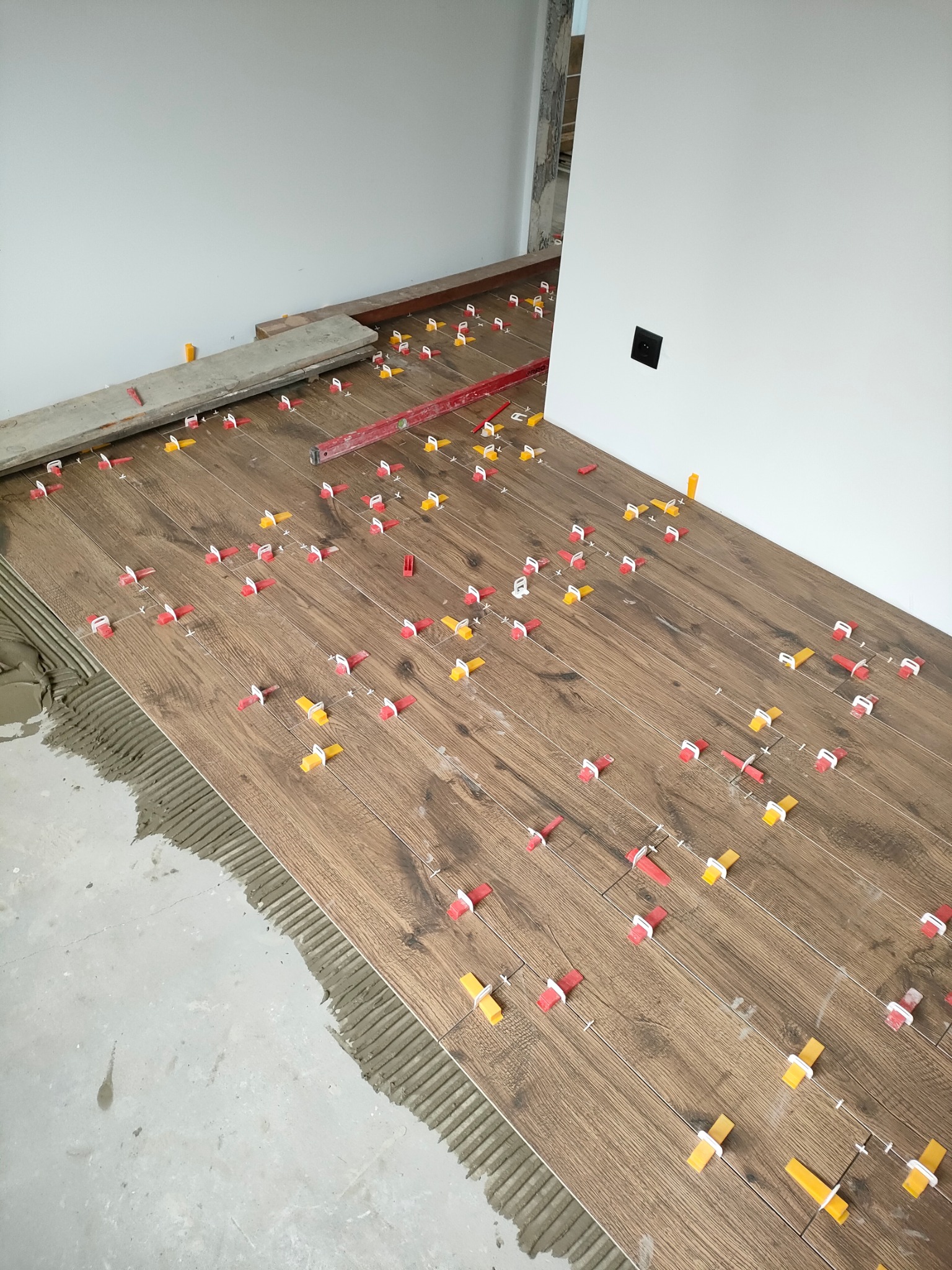 Układanie płytek podłogowych imitujących drewno z użyciem klipsów poziomujących; widoczny fragment podłogi z nałożonym klejem i poziomica.