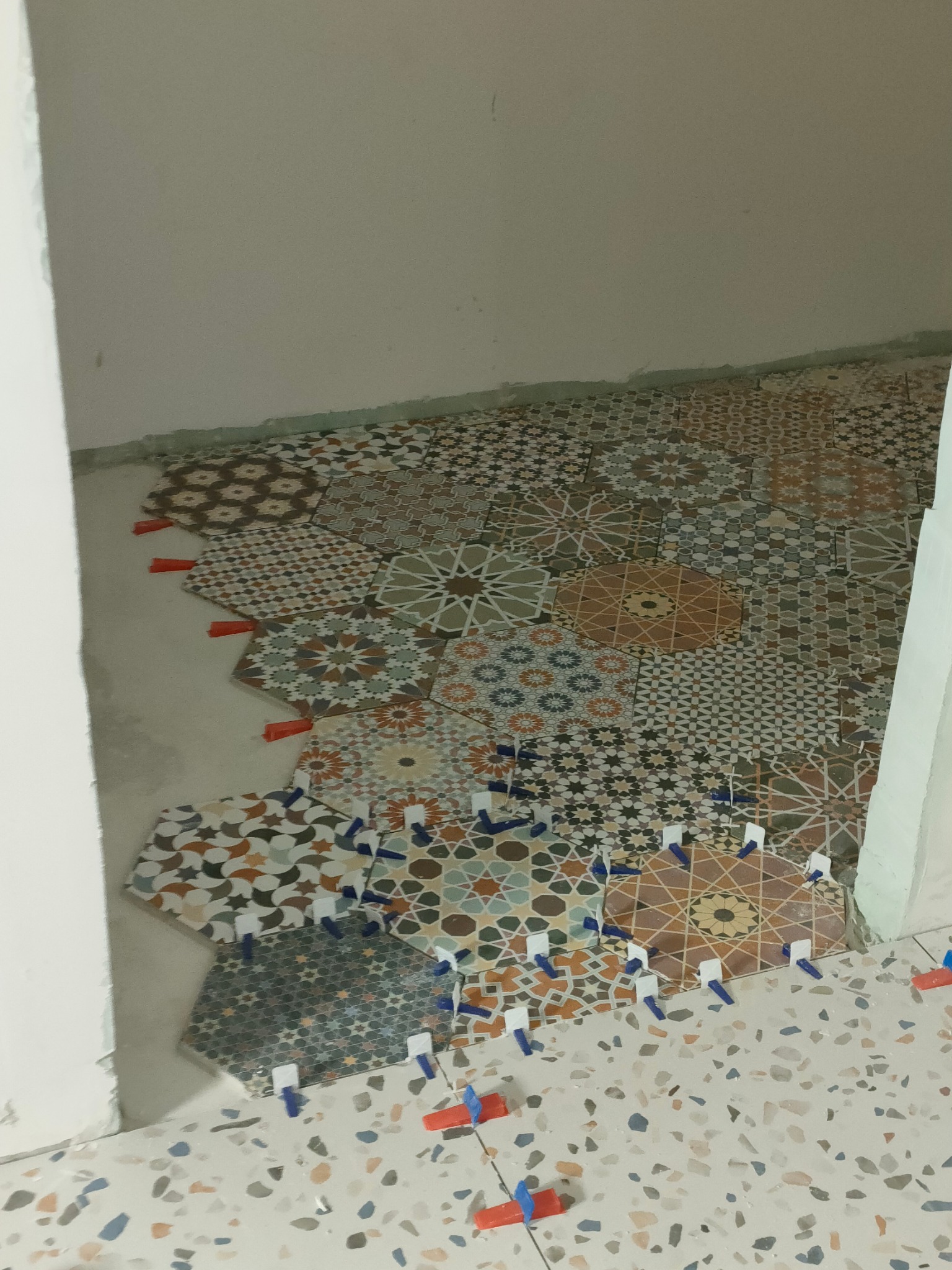 Układanie dekoracyjnych, heksagonalnych płytek podłogowych z użyciem klinów poziomujących. Widoczna surowa ściana w tle.