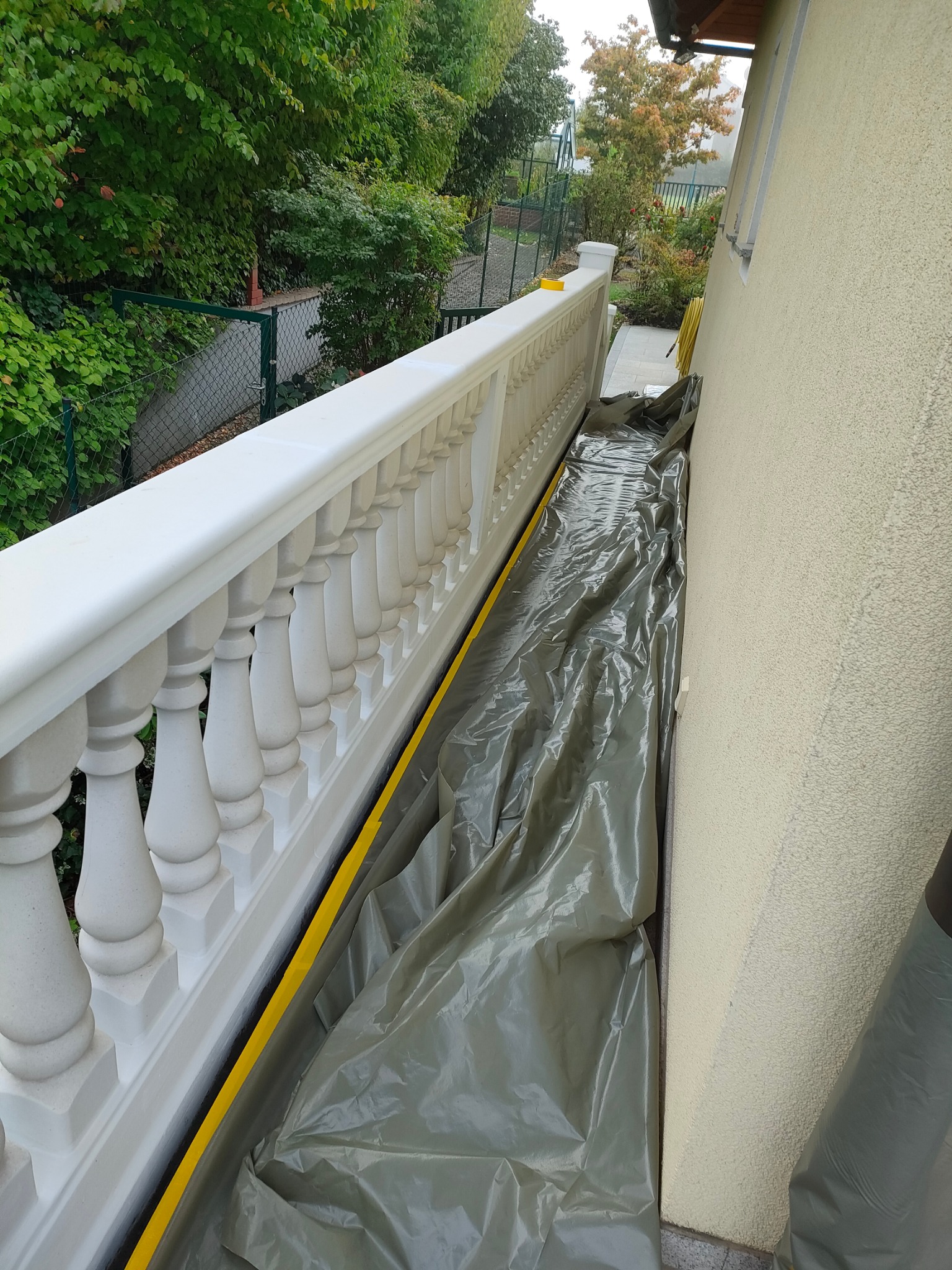 Przygotowanie balkonu z białą balustradą do prac remontowych, zabezpieczony folią i taśmą malarską, widok z góry