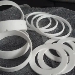 Białe, plastikowe pierścienie i obręcze z otworami na folii bąbelkowej, prawdopodobnie elementy oświetleniowe lub dekoracyjne.