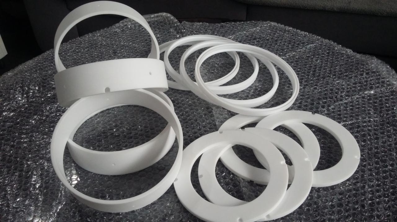 Białe, plastikowe pierścienie i obręcze z otworami na folii bąbelkowej, prawdopodobnie elementy oświetleniowe lub dekoracyjne.