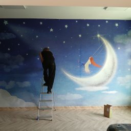 MIWA EKO - Mężczyzna na drabinie montuje fototapetę z motywem księżyca i gwiazd w pokoju. Widoczne narzędzia i karton. Jasne panele podłogowe.