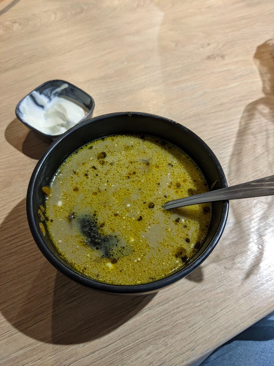 Porcja zupy z dodatkiem ziół i kleksem śmietany w czarnej miseczce obok, widok z góry na drewnianym stole.