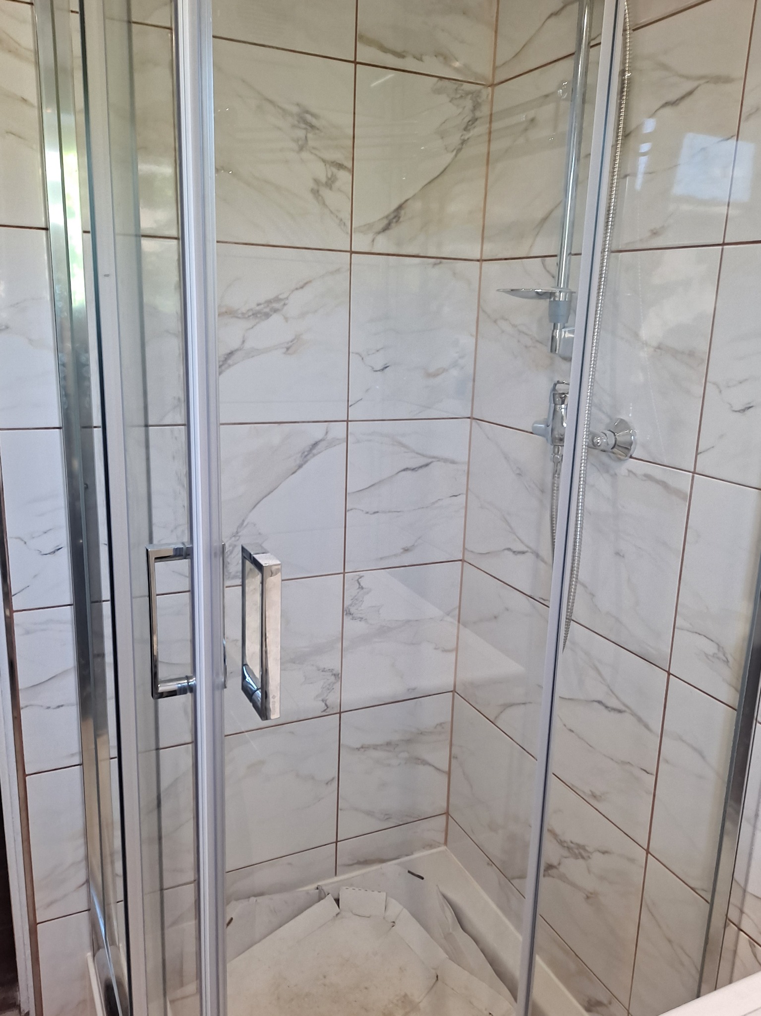 Kabina prysznicowa z chromowanymi detalami i marmurkowymi płytkami na ścianach, widoczne elementy armatury i osłona brodzika.