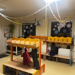 Eureka sp. z. o. o. - Wnętrze szatni przedszkolnej z żółto-pomarańczowymi szafkami na ubrania, udekorowane papierowymi łańcuchami i śnieżynkami na oknach.