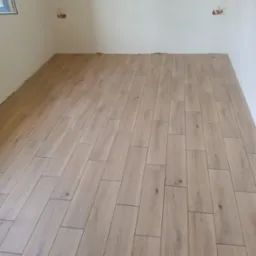 Ułożona podłoga z jasnych paneli imitujących drewno w pustym pokoju z instalacją elektryczną bez osprzętu.