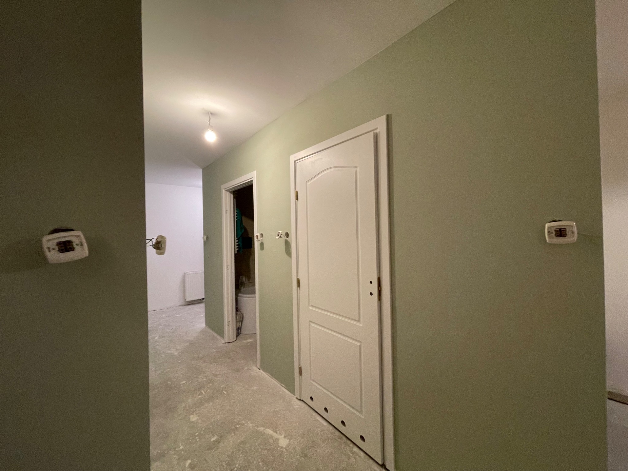 Korytarz w trakcie remontu: ściany pomalowane na oliwkowy kolor, białe drzwi wewnętrzne, surowa podłoga przygotowana do dalszych prac wykończeniowych.