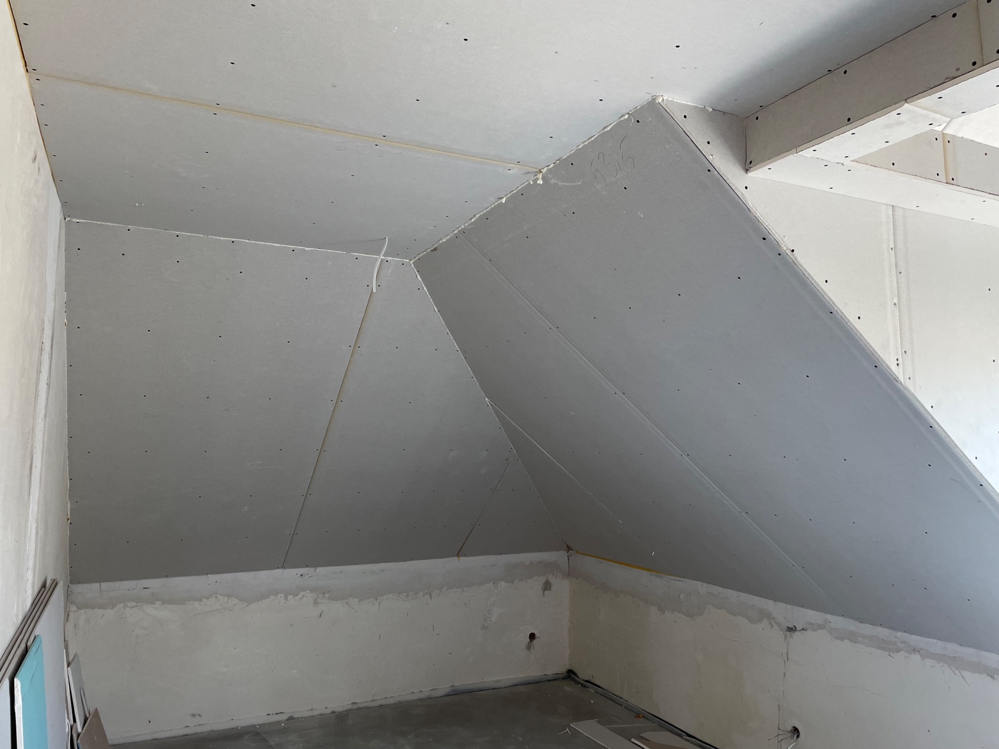 Sufit na poddaszu w trakcie montażu płyt gipsowo-kartonowych, widoczne łączenia płyt i niedoskonałości na ścianach.