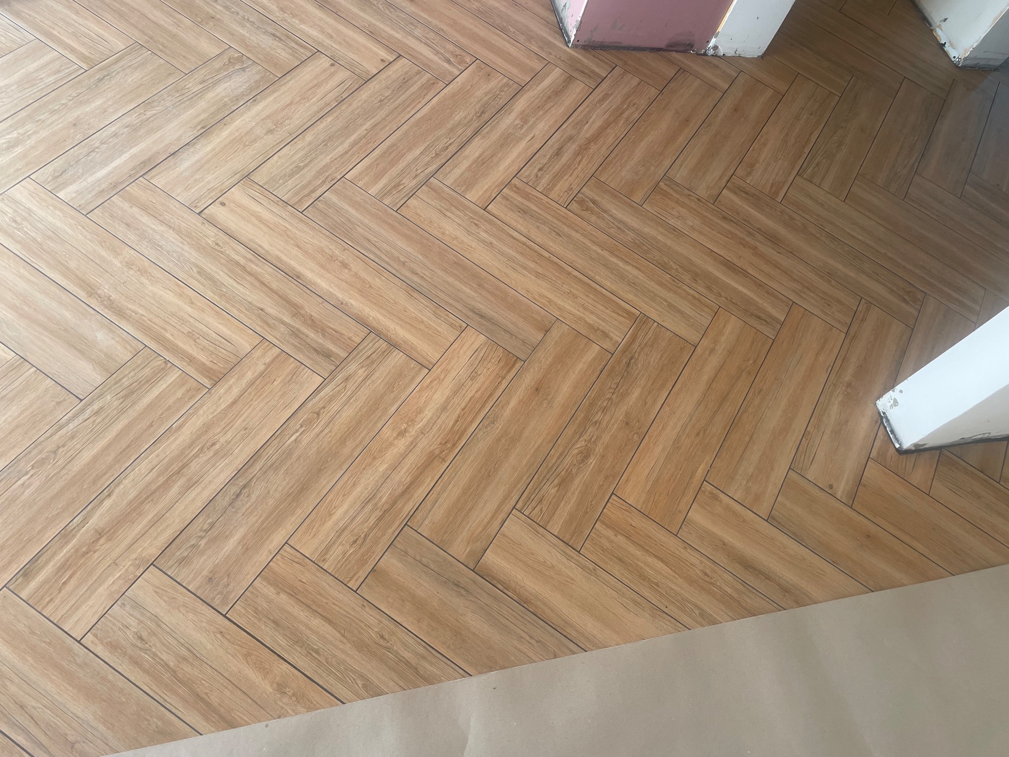 Ułożona w jodełkę podłoga z płytek imitujących drewno, widoczny fragment ściany w trakcie prac wykończeniowych.