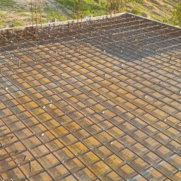 KBB Usługi Ogólnobudowlane - Siatka zbrojeniowa ułożona na szalunku z desek przed zalaniem betonem, widok z góry, z pojazdem i zielenią w tle.