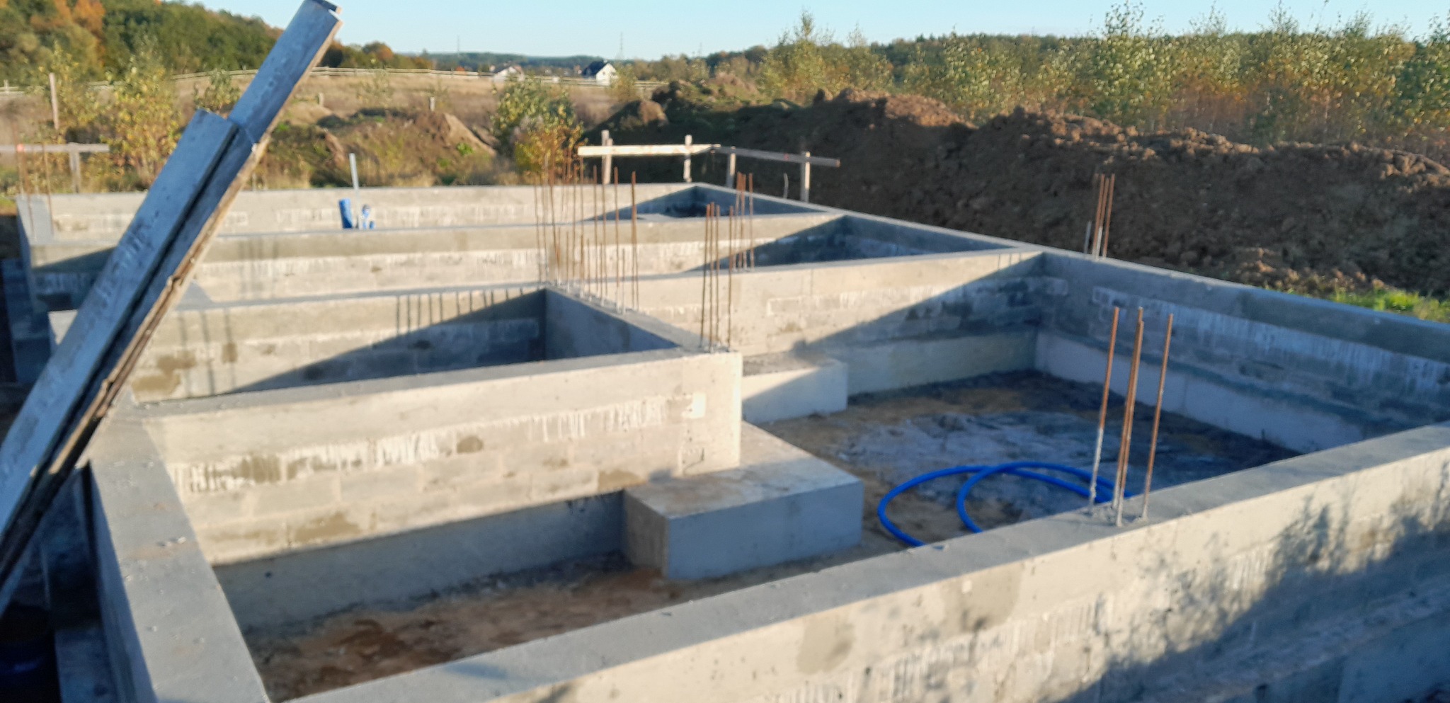 Wylane betonowe fundamenty domu jednorodzinnego z wystającymi prętami zbrojeniowymi, widok z góry na plac budowy w słoneczny dzień.