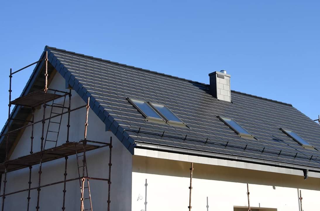 Nowy, grafitowy dach z trzema oknami połaciowymi i kominem wentylacyjnym, widziany z rusztowania w Wejherowie.