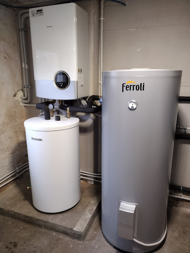 Kompaktowa instalacja grzewcza w kotłowni: wiszący piec gazowy Hisense z okrągłym wyświetlaczem, biały zasobnik ciepłej wody Buderus i szary zasobnik Ferroli z widocznym termometrem, połączone...