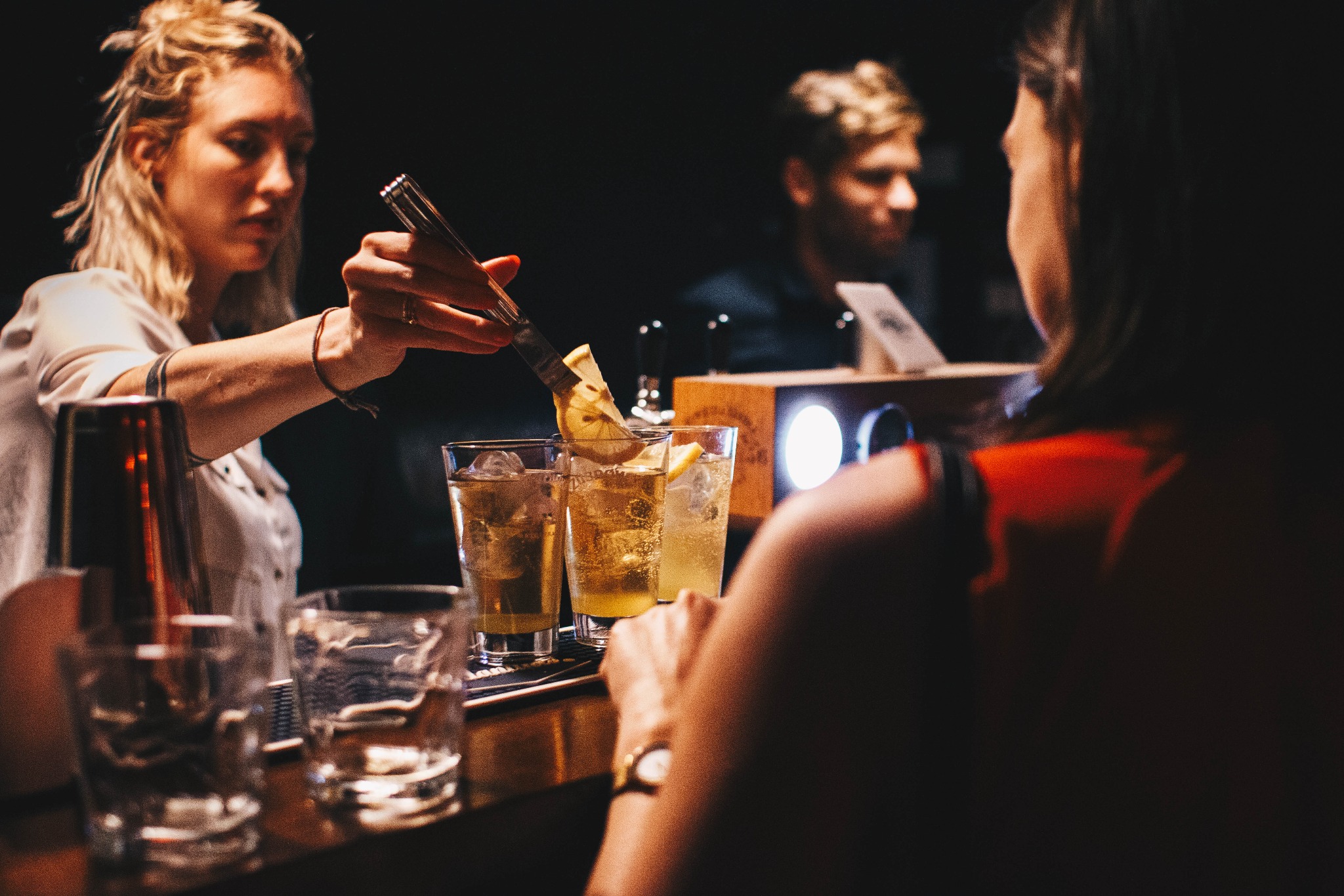 Barmanka dodaje plasterek cytryny do drinka z lodem przy barze, w tle klient