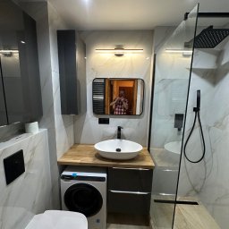 DomExpert Wrocław - Nowoczesna łazienka z kabiną prysznicową typu walk-in, umywalką nablatową i pralką. Marmurowe płytki, czarne akcenty i oświetlenie punktowe.