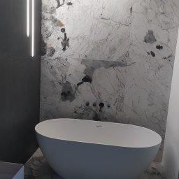 DomExpert Wrocław - Nowoczesna łazienka z wolnostojącą wanną o owalnym kształcie, wykończona płytkami imitującymi marmur z wyraźnymi czarnymi i brązowymi żyłami, oświetlona liniowymi lampami LED na suficie i ścianie.