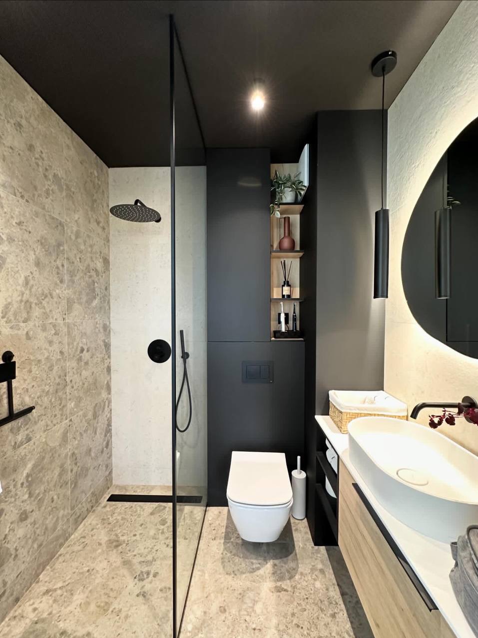 Nowoczesna łazienka z kabiną prysznicową typu walk-in, umywalką nablatową i czarnymi akcentami, w tym armaturą i oświetleniem. Marmurowe płytki na podłodze i ścianach.