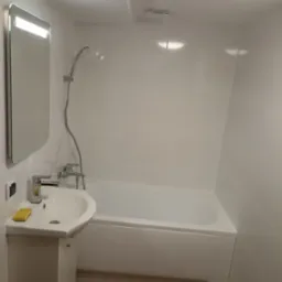 Nowoczesna łazienka z białymi płytkami, umywalką na szafce z mydłem, wanną i podświetlanym lustrem.