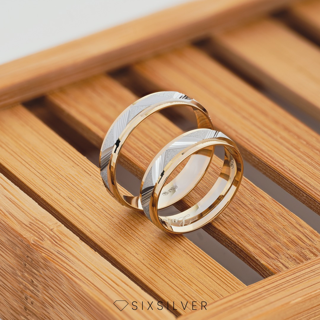 Dwa złote obrączki z geometrycznym wzorem na drewnianej tacy, oferowane w Gliwicach, z widocznym logo firmy.