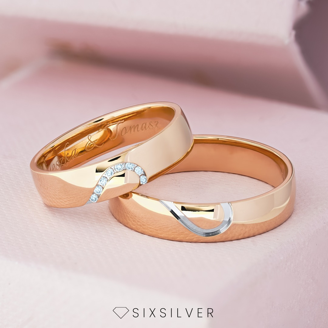 Dwa złote pierścionki ślubne na różowym tle, jeden z wygrawerowanymi imionami i rzędem małych diamentów, drugi z wyciętym znakiem nieskończoności wypełnionym srebrem.