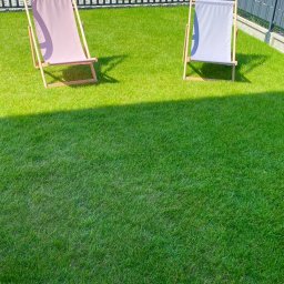 Your Smart Garden Sp. z o.o. - Równy trawnik z dwoma leżakami w odcieniach różu i szarości, ogrodzony czarnym metalowym płotem i szarą osłoną z logo Smart Garden.