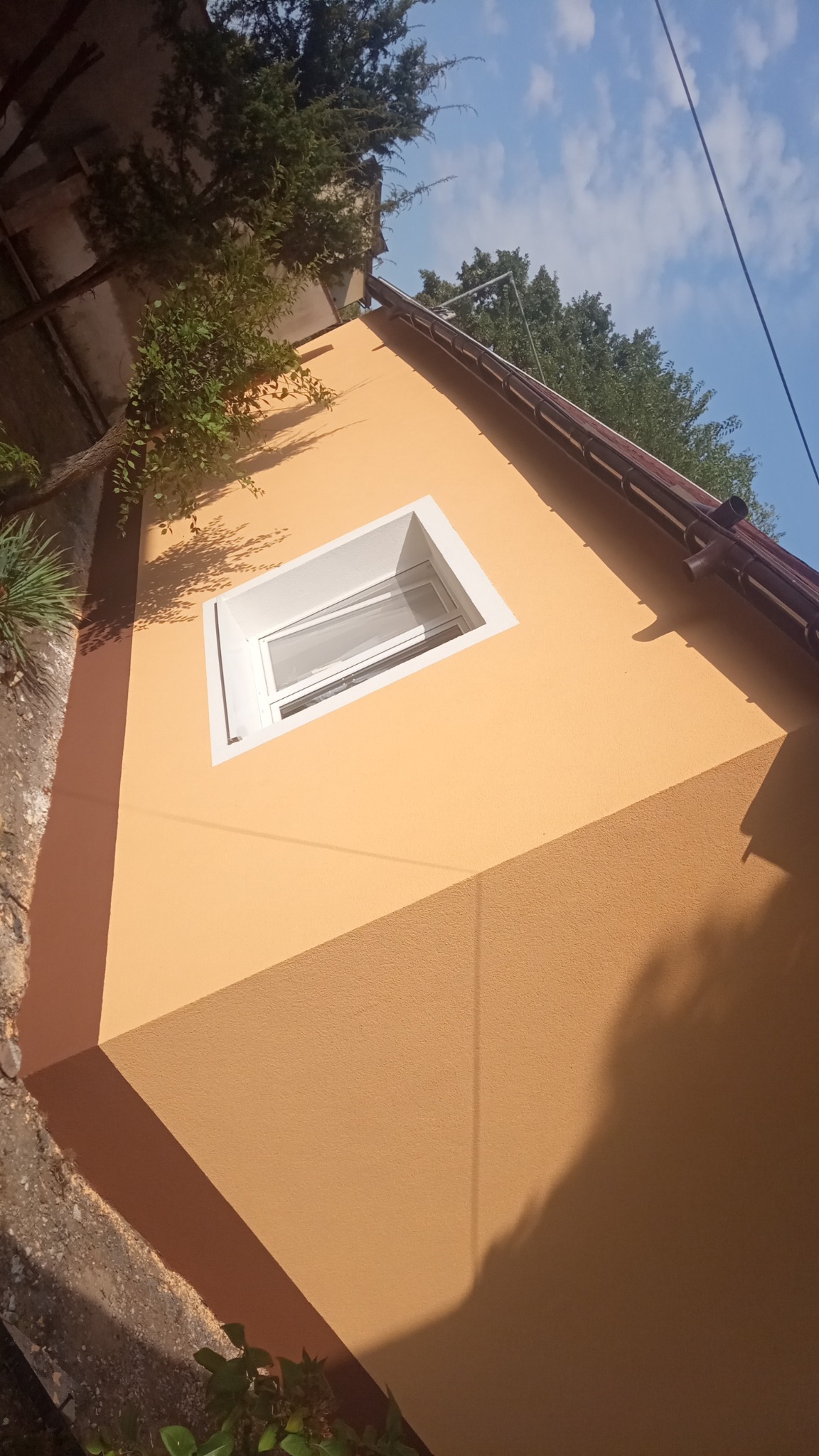 Ocieplona elewacja budynku z oknem w białej ramie, widok z dołu, cień drzewa na ścianie.