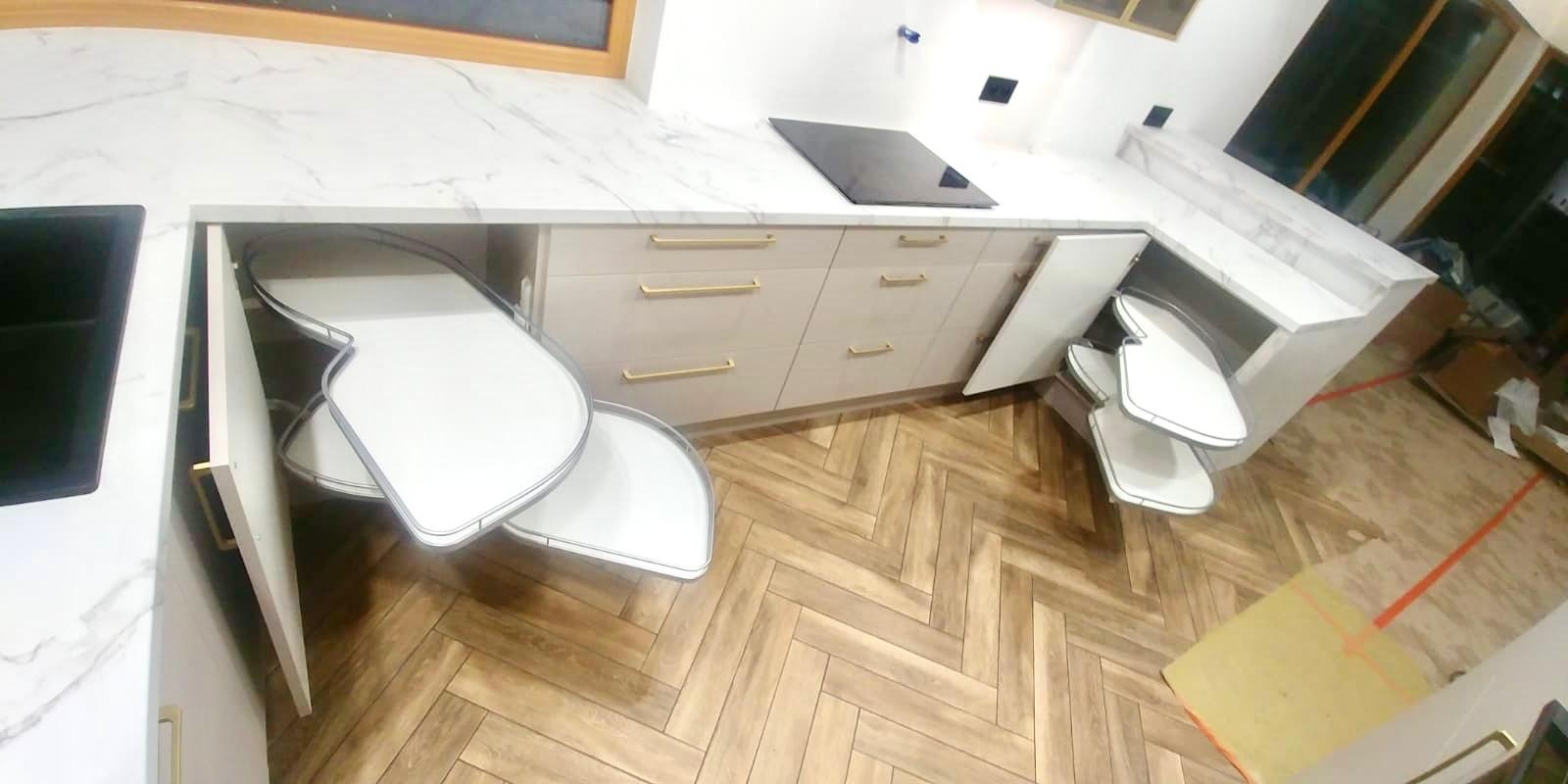 Jasna kuchnia na wymiar z marmurowym blatem, złotymi uchwytami i wysuwanymi półkami narożnymi typu nerka, widok z góry, parkiet w jodełkę.