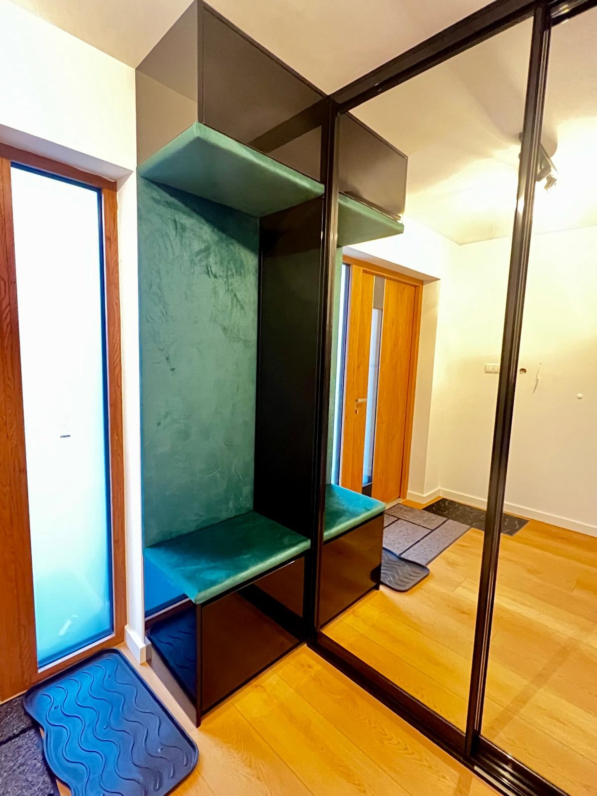 Przedpokój z zabudową: czarna szafa przesuwna z lustrem i siedziskiem obitym zielonym welurem, widoczne wejście do pokoju.