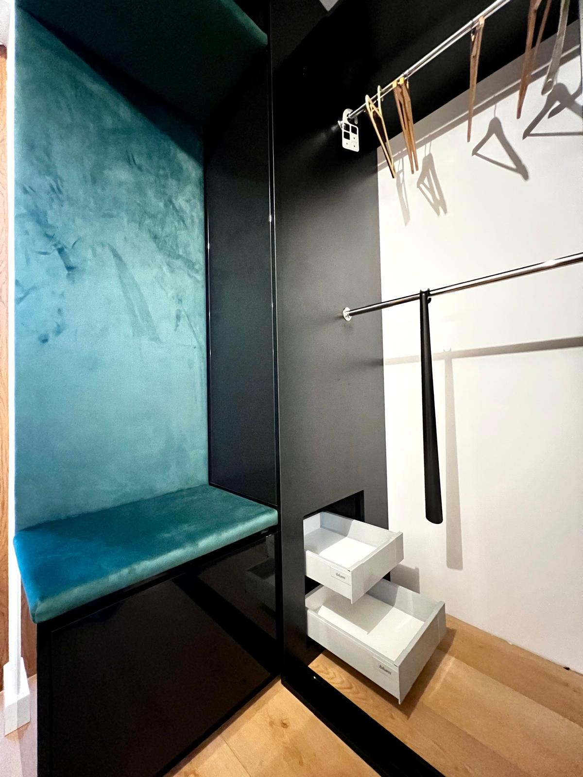 Wnętrze garderoby z siedziskiem obitym turkusowym welurem, wysuwanymi szufladami marki Blum i drążkiem na wieszaki.