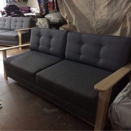 Fuerte - Dwa modułowe, tapicerowane, szare fotele z drewnianymi podłokietnikami; w tle widoczny narożnik w tym samym stylu, całość w warsztacie.