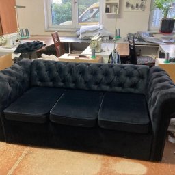 Fuerte - Czarna, welurowa sofa typu Chesterfield w warsztacie, widoczne maszyny do szycia i materiały tapicerskie w tle.