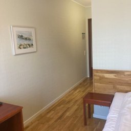 Fuerte - Pokój hotelowy z drewnianą podłogą, stolikiem nocnym i obrazem na ścianie w stonowanych kolorach.