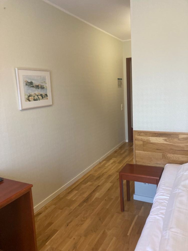 Pokój hotelowy z drewnianą podłogą, stolikiem nocnym i obrazem na ścianie w stonowanych kolorach.