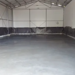 Wnętrze hali z nową, gładką, szarą posadzką przemysłową zabezpieczoną folią przy ścianach.