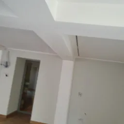 Wnętrze po malowaniu na biało, widoczne świeżo pomalowane ściany, sufit z elementami konstrukcyjnymi i fragment podłogi z drewna.