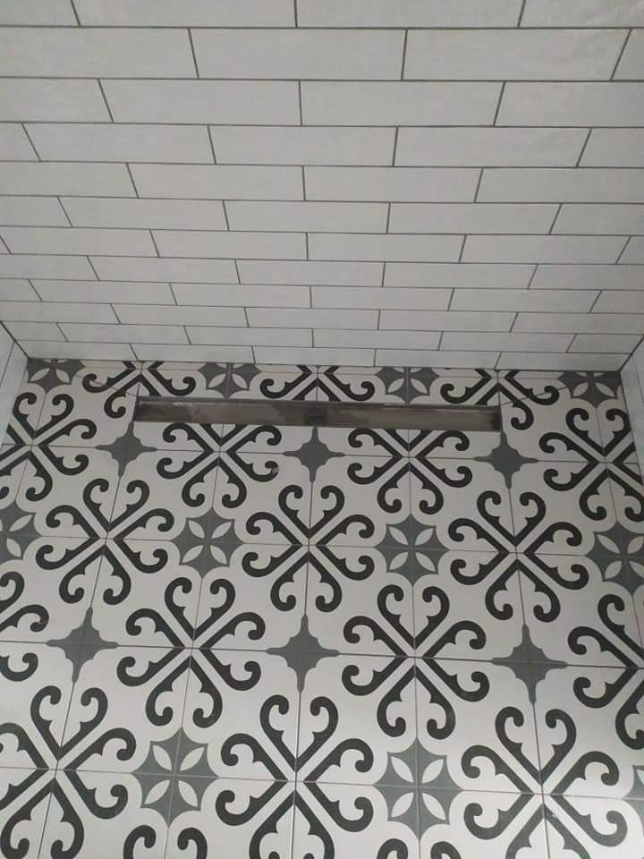 Wykończona łazienka z wzorzystą, czarno-białą podłogą z odpływem liniowym i białymi, prostokątnymi płytkami na ścianie, ułożonymi w cegiełkę.