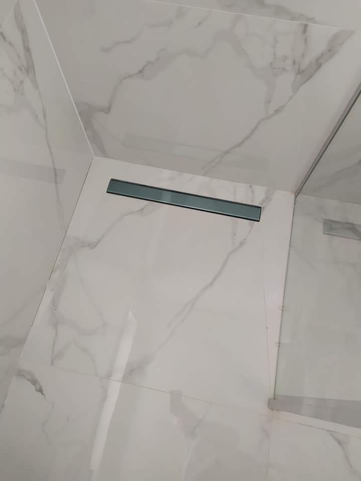 Białe marmurowe płytki w kabinie prysznicowej z liniowym odpływem podłogowym.