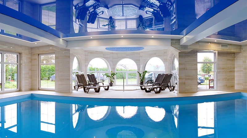 Błękitny, lustrzany sufit w hali basenowej z oknami i leżakami, odbicie w wodzie.