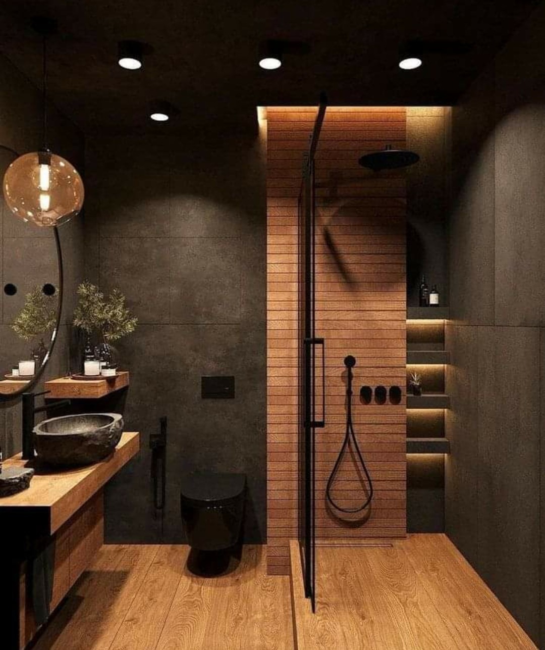 Nowoczesna łazienka w ciemnych kolorach z drewnianymi akcentami: kamienna umywalka na drewnianym blacie, czarna toaleta, kabina prysznicowa z drewnianą ścianą i podświetlanymi półkami.