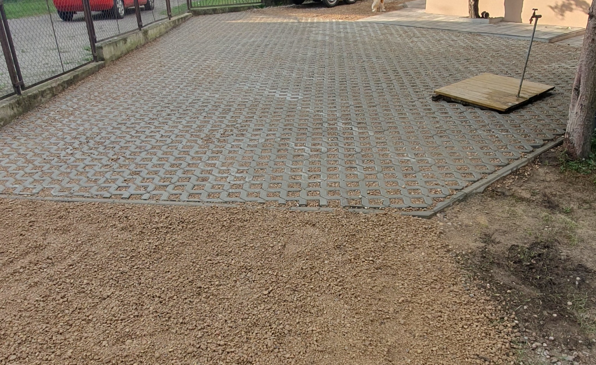 Ułożona szara ażurowa kostka brukowa na podjeździe, częściowo wypełniona drobnym żwirem, z widocznym fragmentem terenu przygotowanego pod dalsze prace.