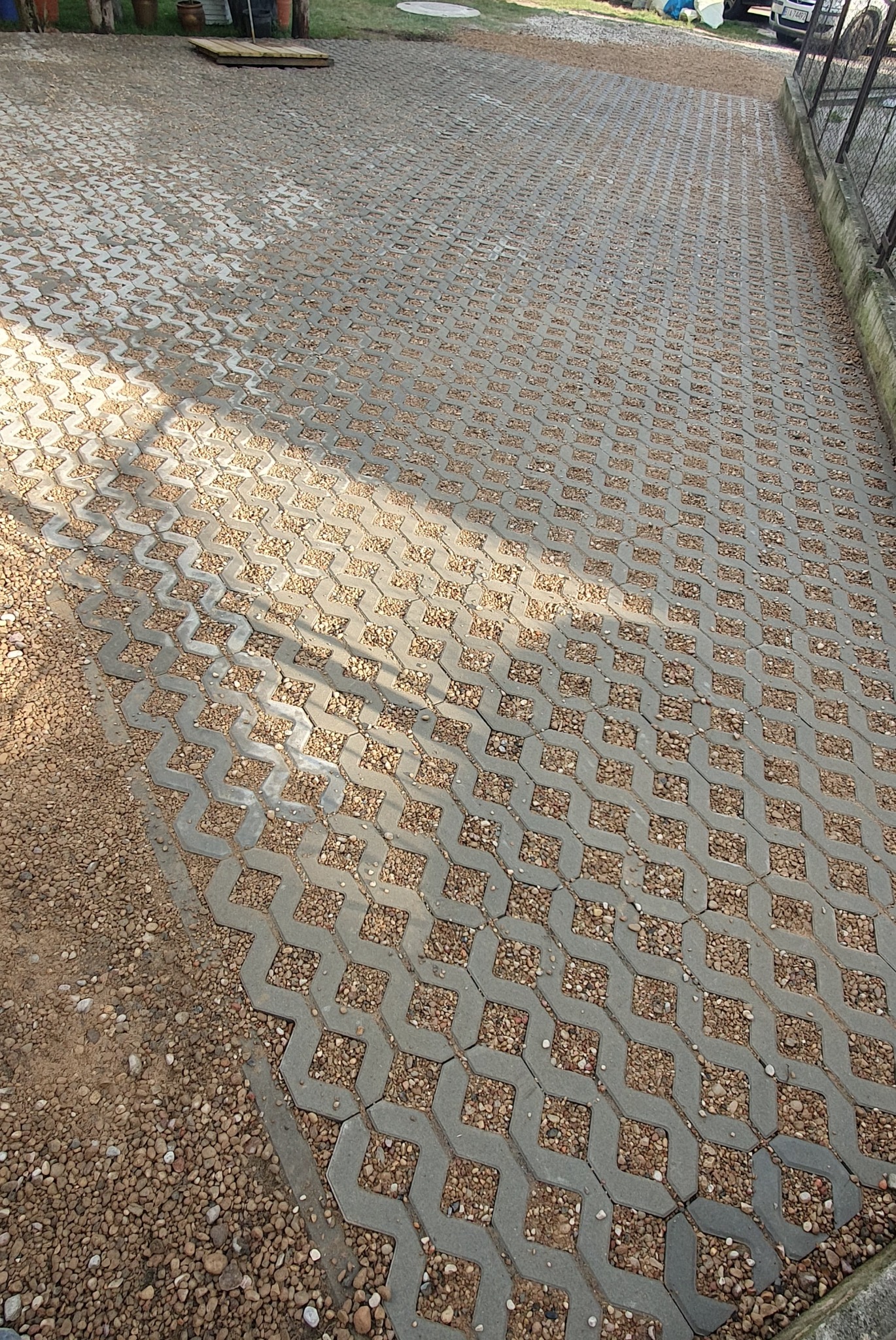 Ułożona szara kostka ażurowa z wypełnieniem żwirowym tworzy nawierzchnię podjazdu, widoczna krawędź z drobnym żwirem i fragment ogrodzenia.